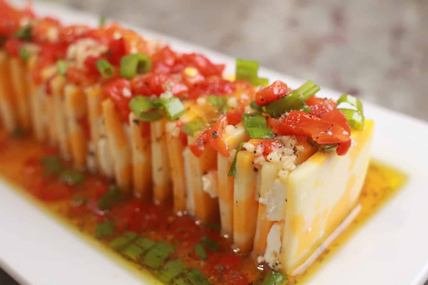 Marinated cheese southern living- slices of cheese stacked on a white platter with a marinated poured over the top