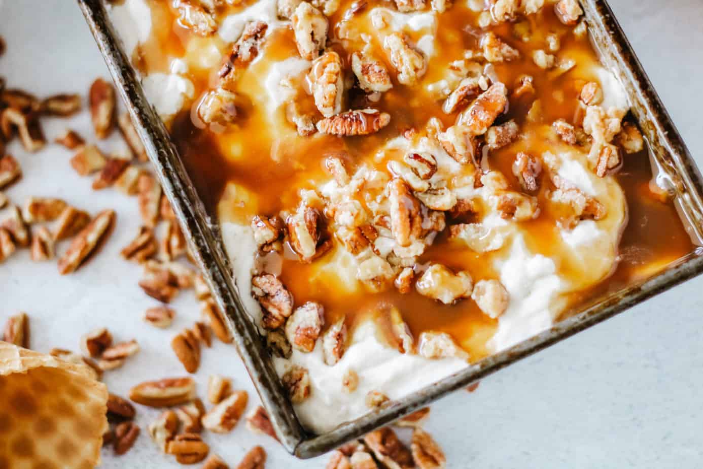 A loaf pan of Pralines and Cream Ice Cream drizzled with caramel sauce and candied praline pecans.