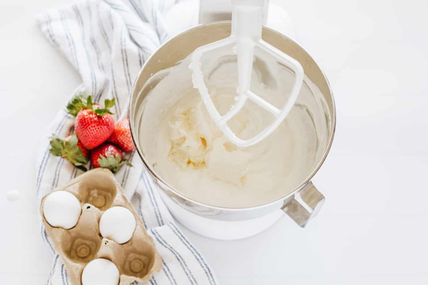 whipping cream cheese and powdered sugar in a glass mixing bowl with whipped cream