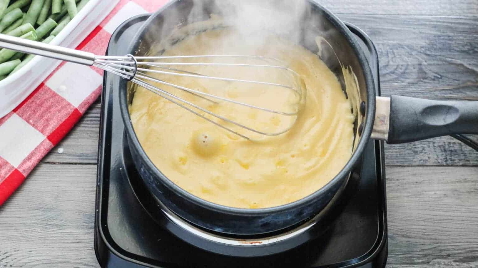 Melted heavy cream, cheeses, and seasonings in a saucepan with a whisk