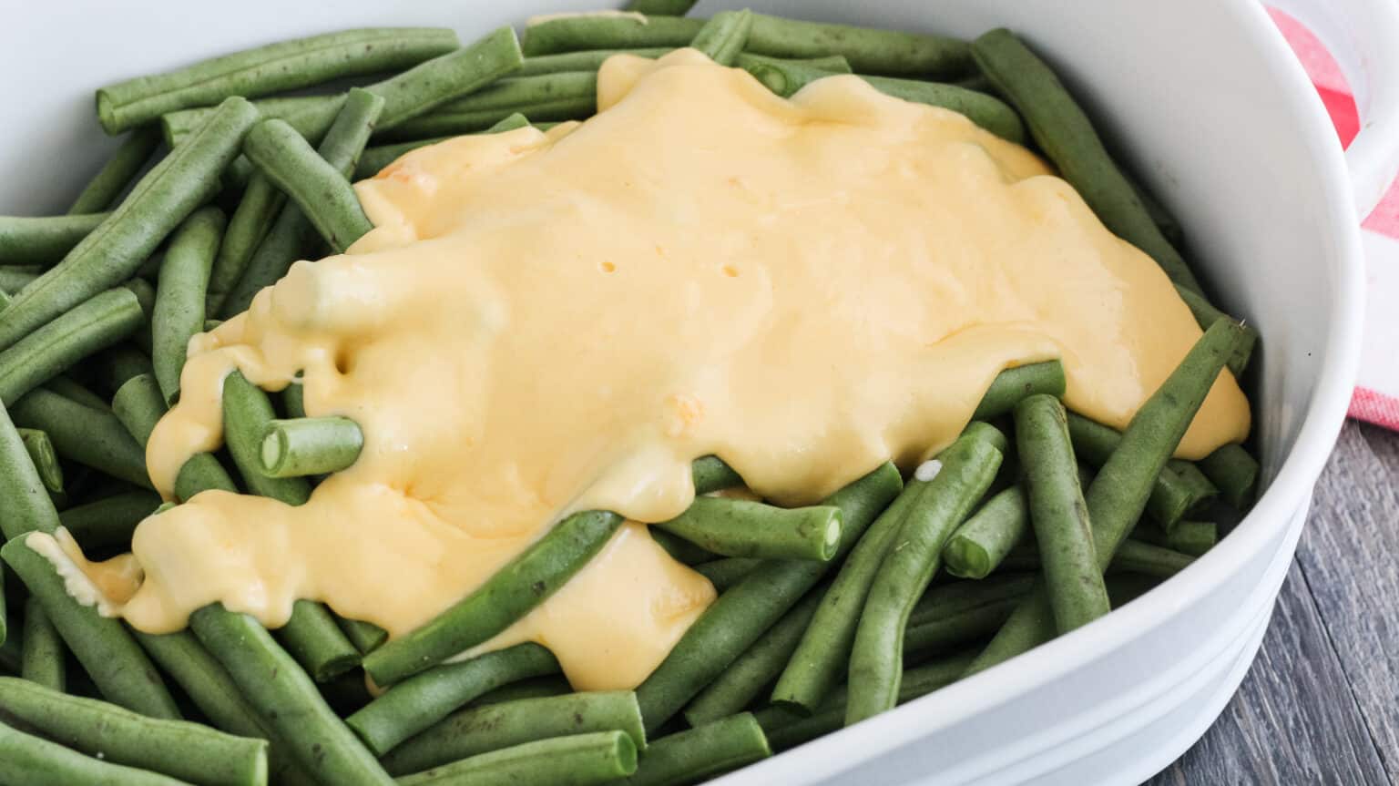 cheese sauce poured over fresh green beans in a white dish