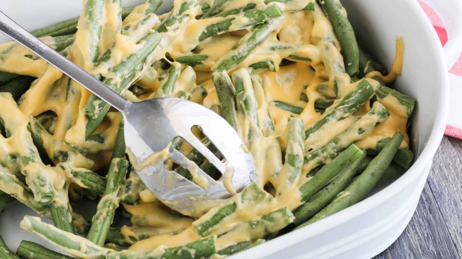 cheese sauce poured over fresh green beans in a white dish and mixed up