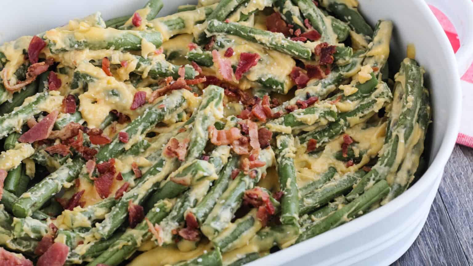 cheese sauce poured over fresh green beans in a white dish with bacon and salt on top