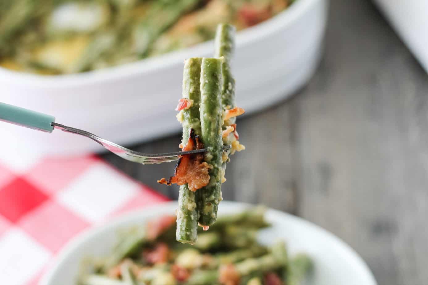 a bite of cheesy green bean casserole  on a white plate with a fork with a few beans on it