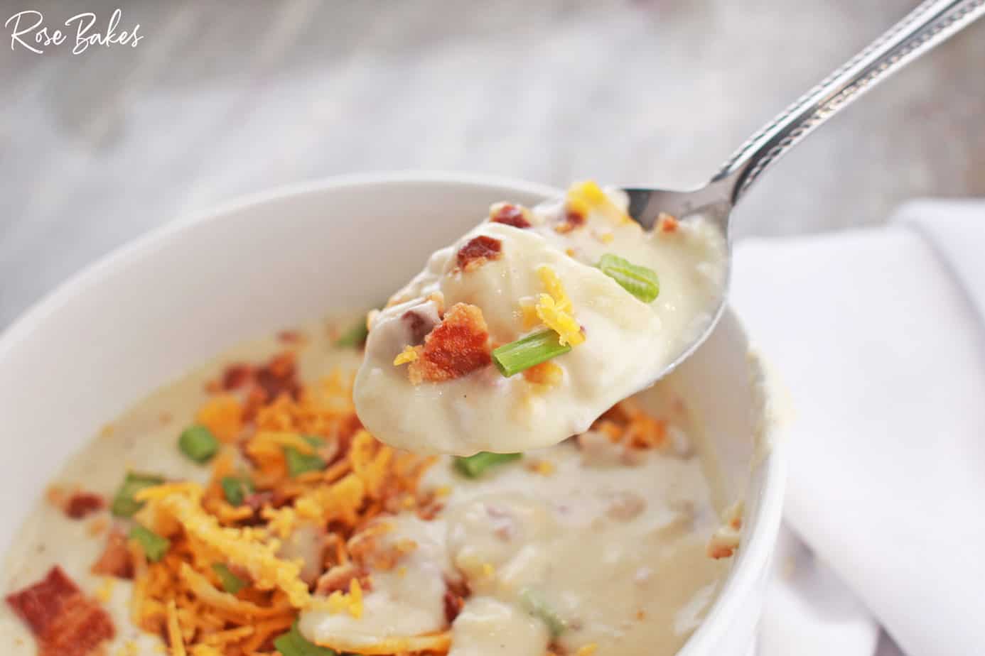 a spoonful of red potato soup with cream cheese in a bowl with bacon and cheese on top and crackers on the side