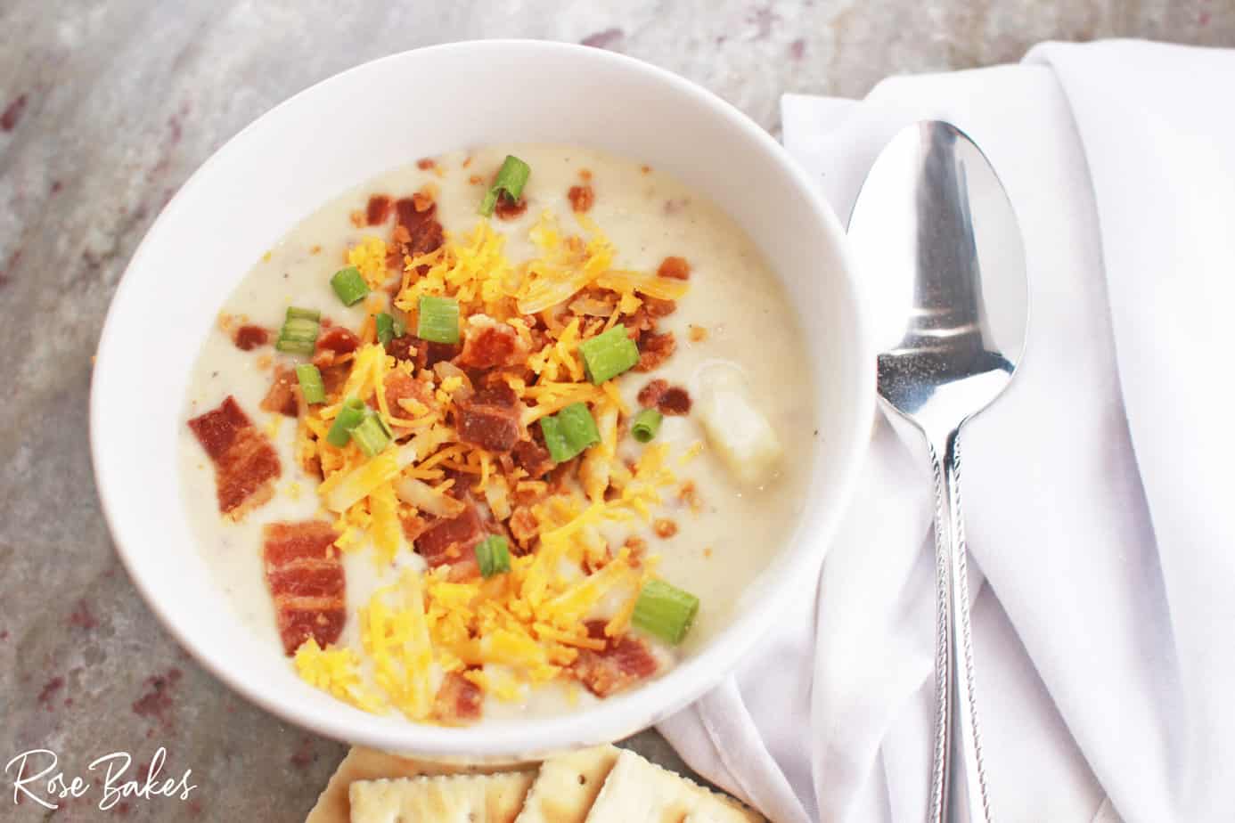 potato soup with cream cheese in a white bowl with bacon and cheese on top and crackers on the side