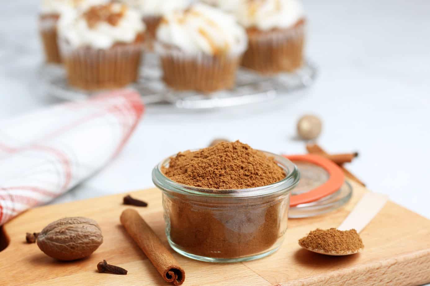 pumpkin pie spice ingredients in a small clear bowl on a cutting board with cupcakes in the background