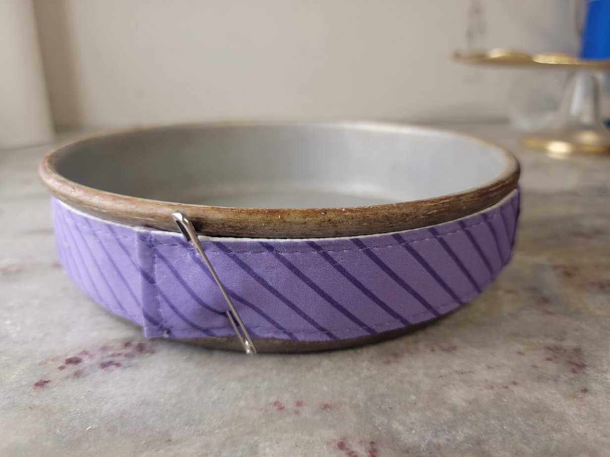 Cake strips wrapped around a cake pan secured with a safety pin