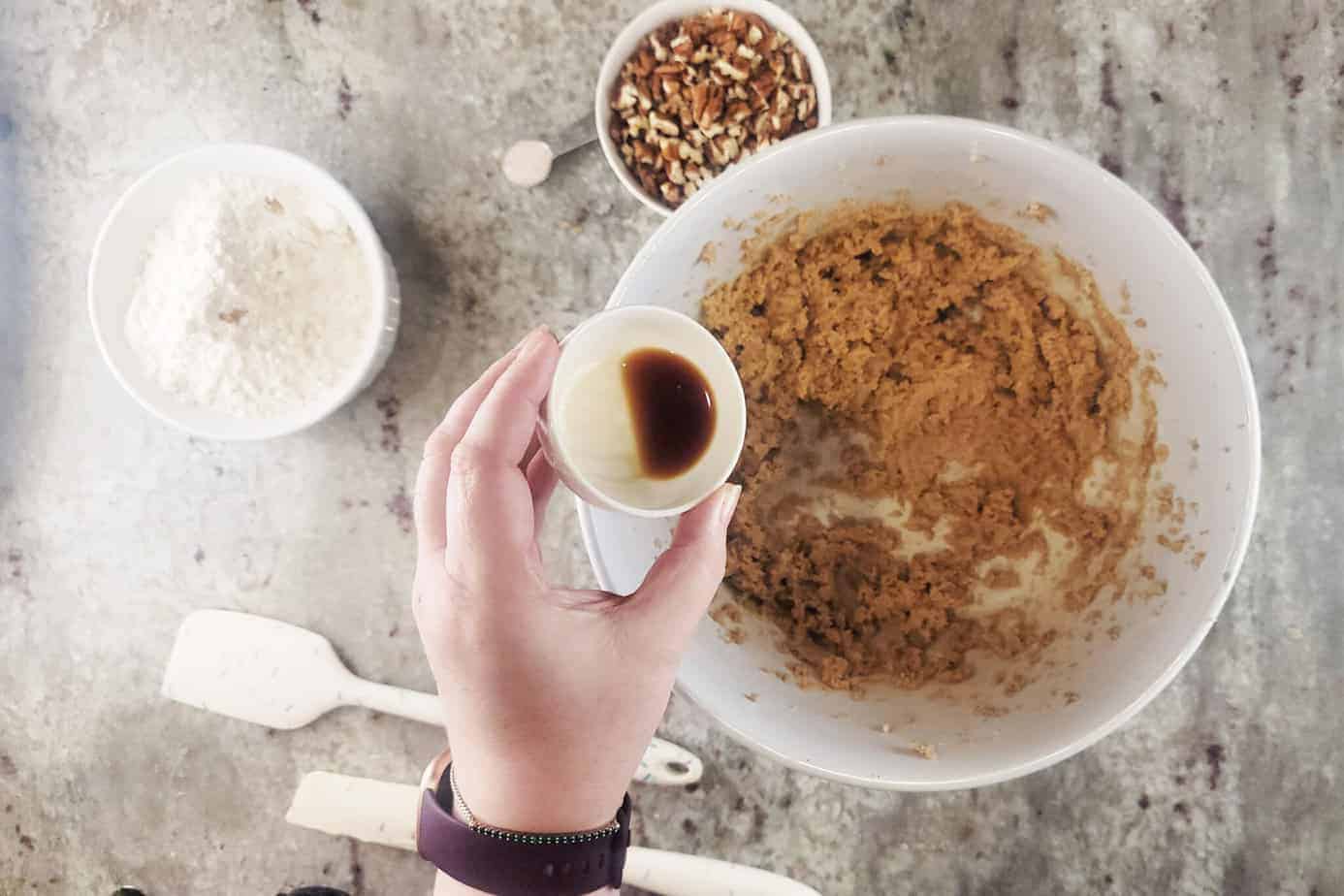 adding vanilla to bowl of ingredients for ingredients for Pecan Praline Cookies 
