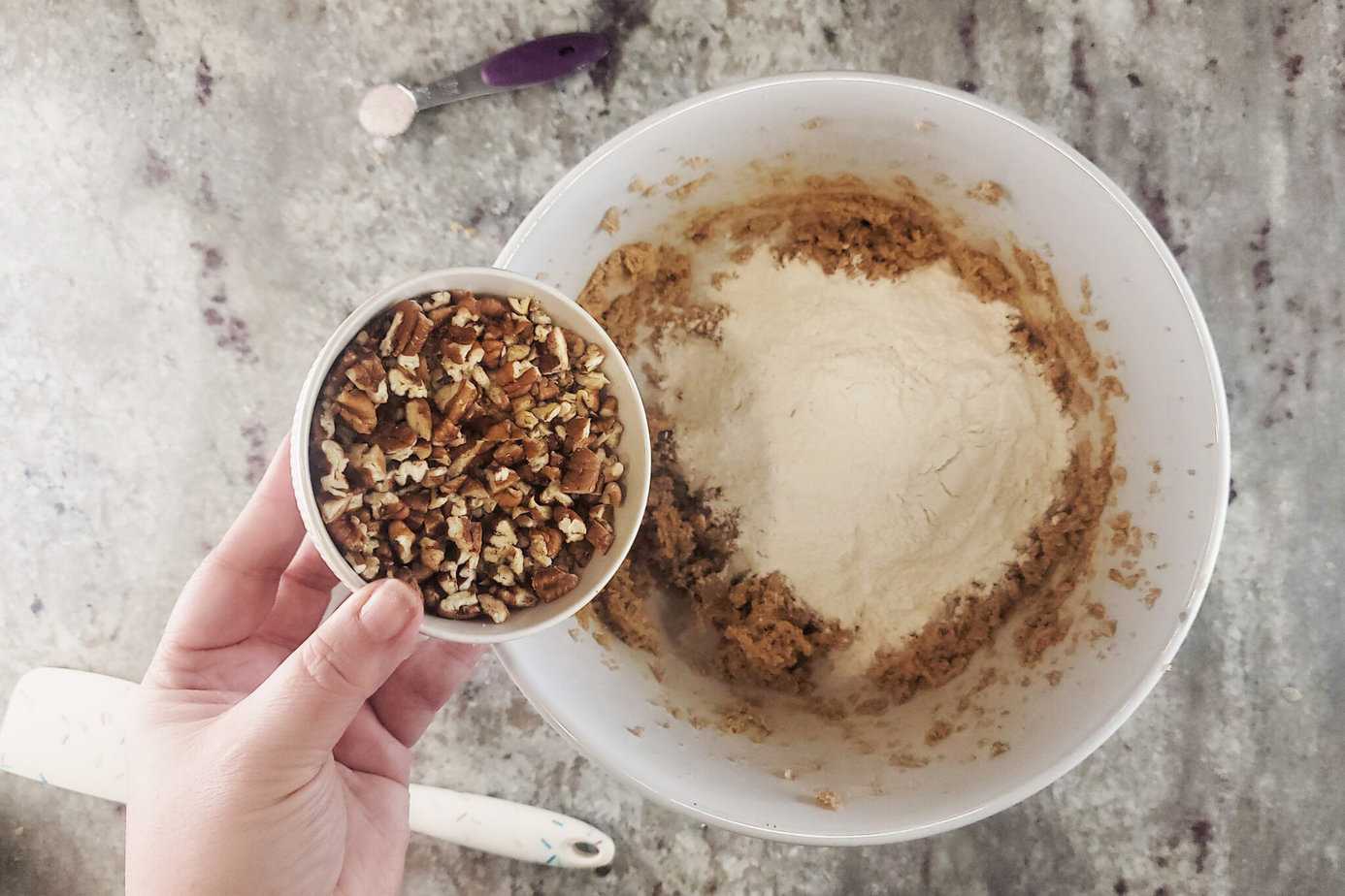adding chopped pecans to large white bowl