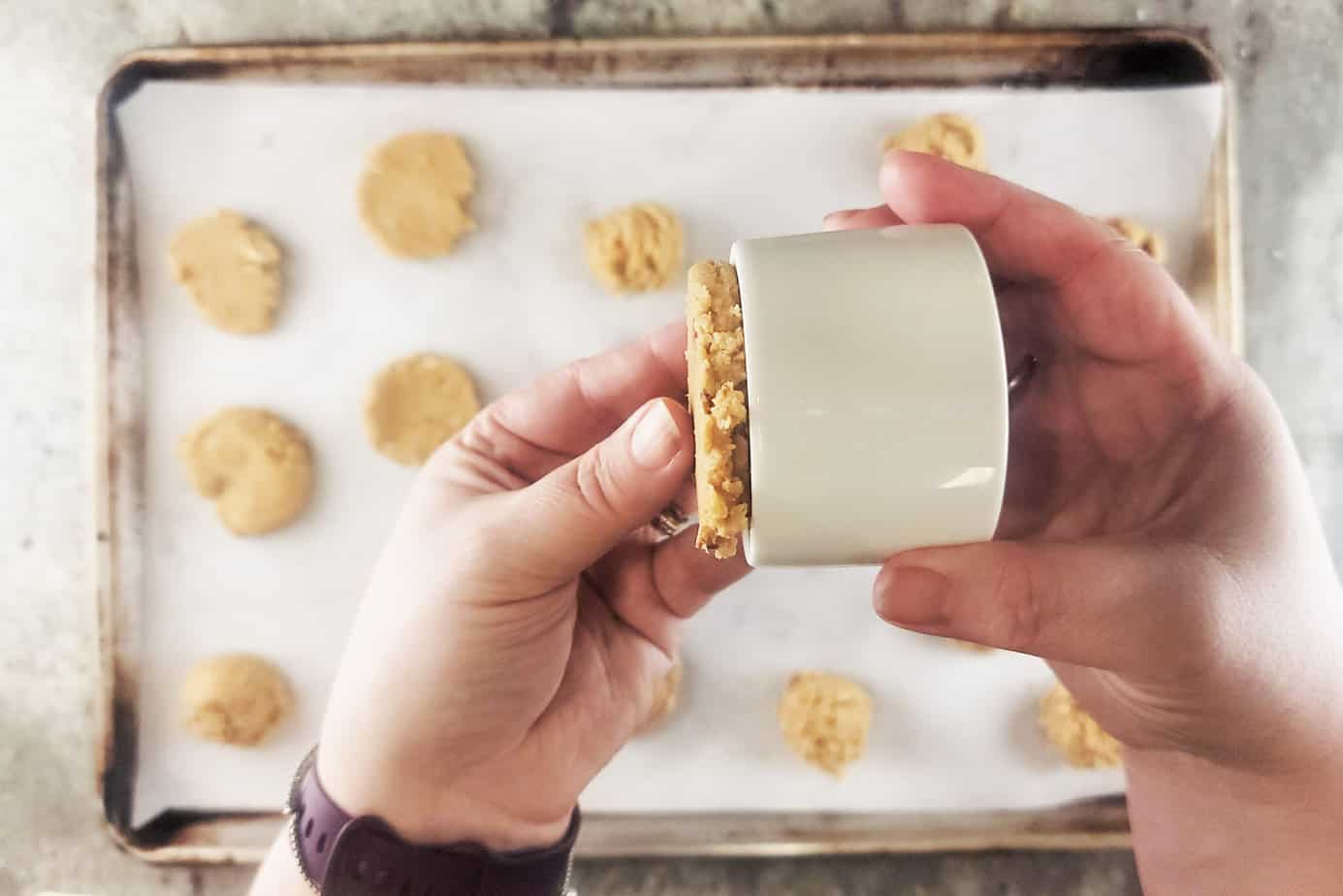 using a ramekin to flatten balls of Pecan Praline Cookies dough on a cookie sheet