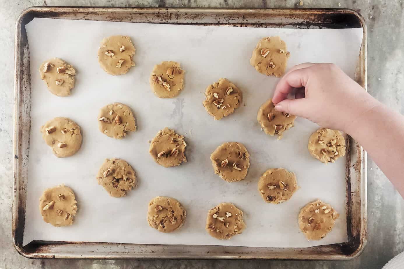 adding extra pecans to the top of scoop of Pecan Praline Cookies dough 