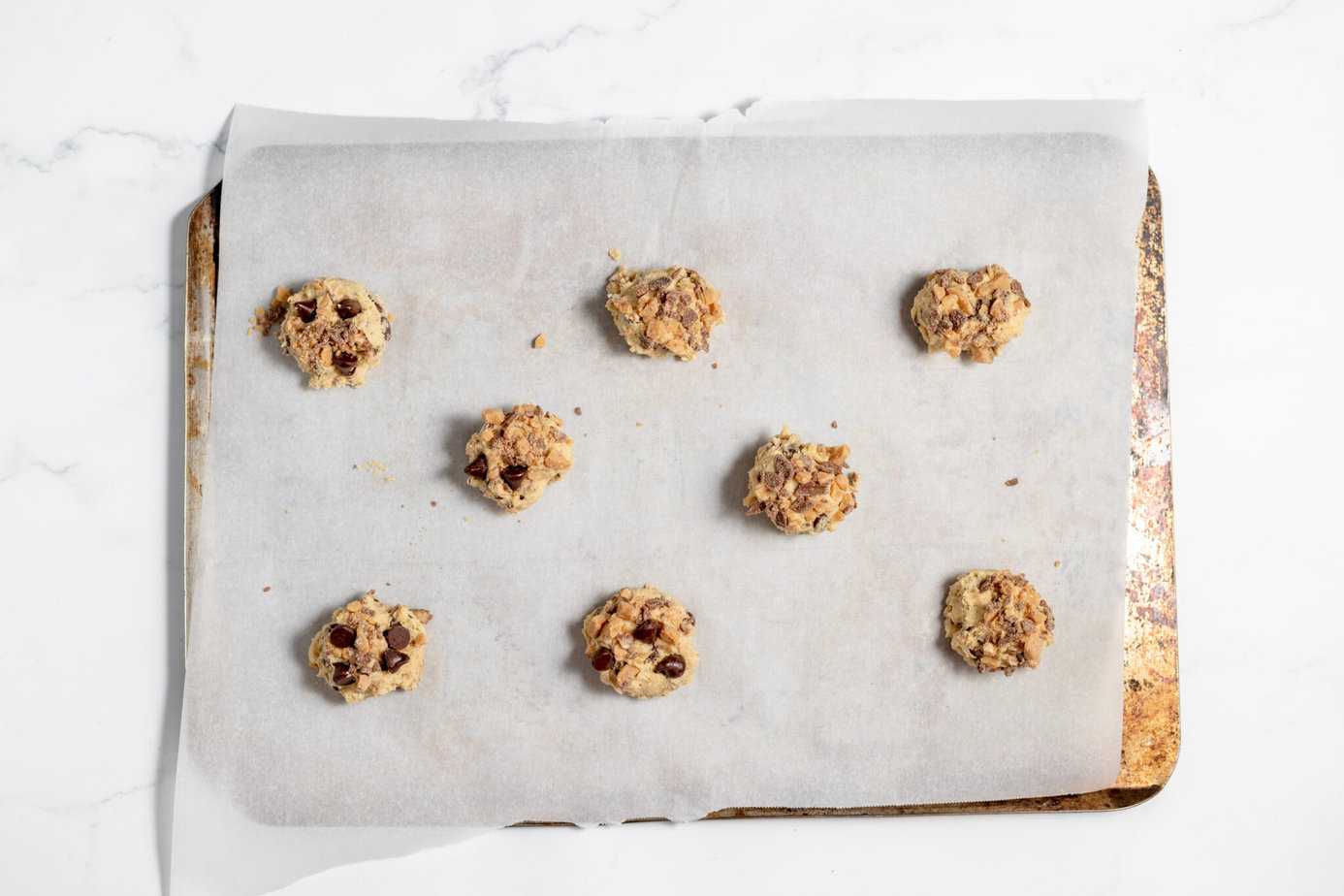 balls of cookie dough on a cookie sheet with parchment with extra chips on top