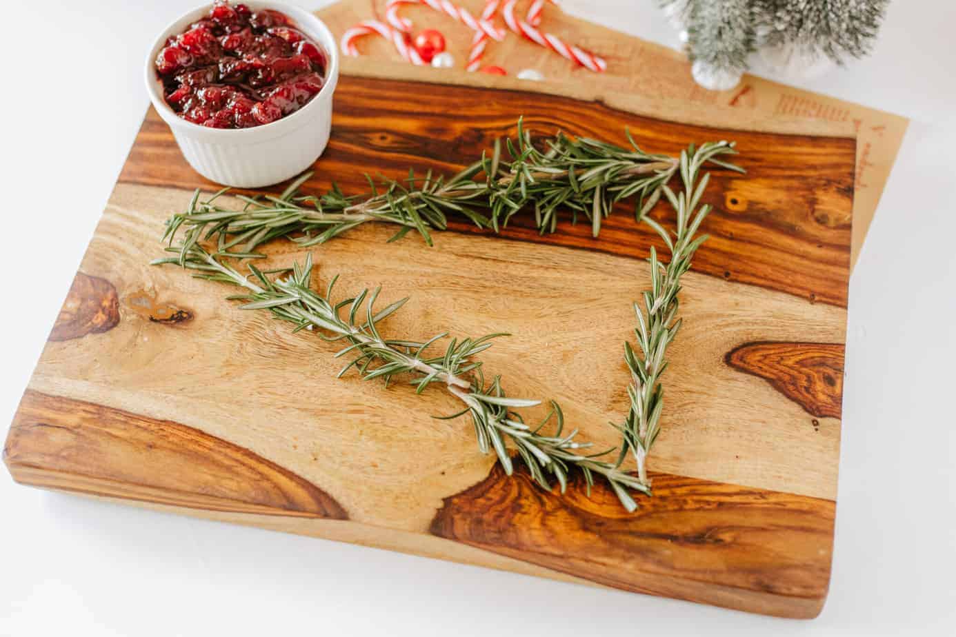 cutting board with rosemary sprigs in shape of christmas tree on a cutting board with bowl of cranberry sauce