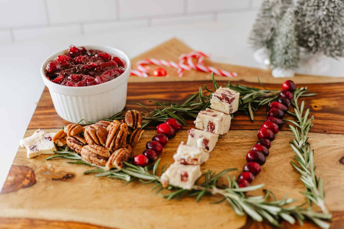adding cranberries to cutting board with rosemary sprigs in shape of christmas tree on a cutting board with bowl of cranberry sauce