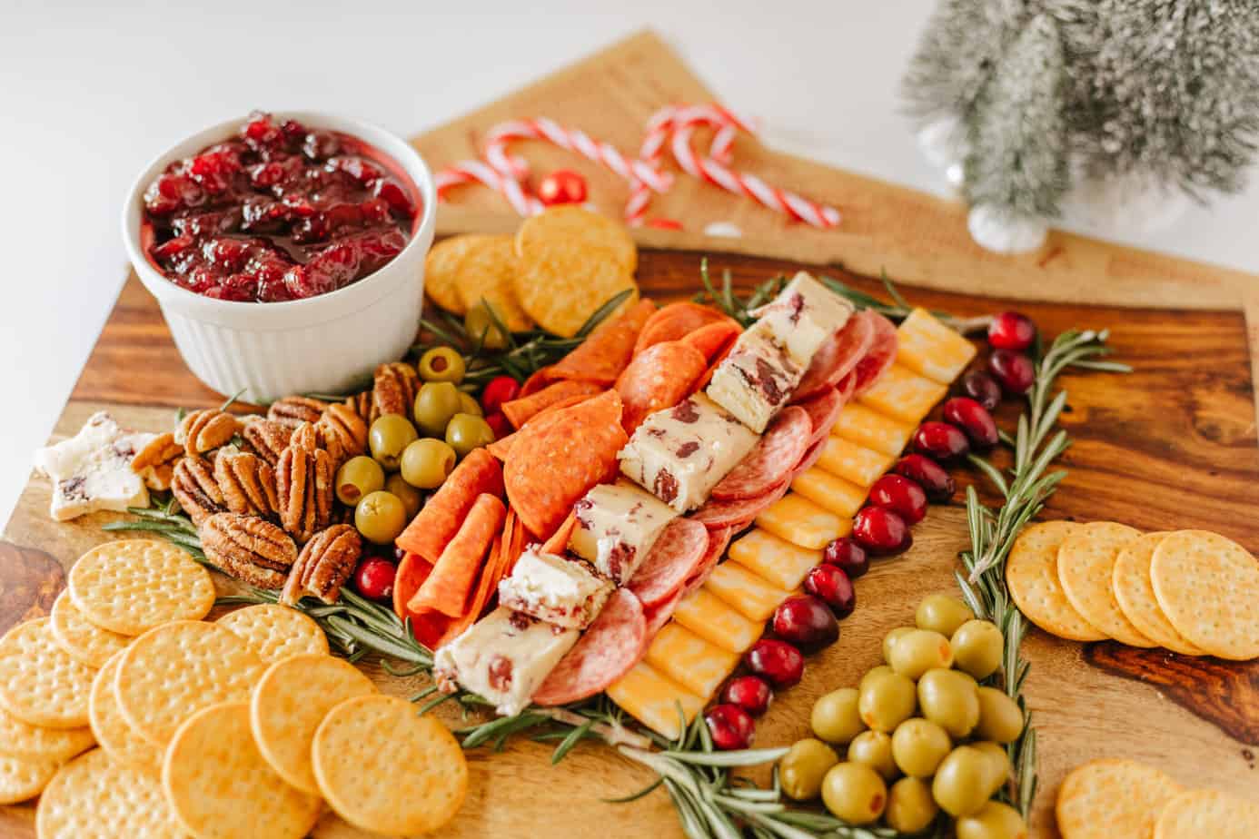 adding salami to cutting board with rosemary sprigs in shape of christmas tree on a cutting board with bowl of cranberry sauce for Christmas Tree Charcuterie board