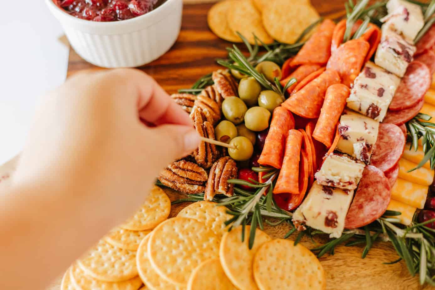 poking an olive with a toothpick on a Christmas charcuterie board