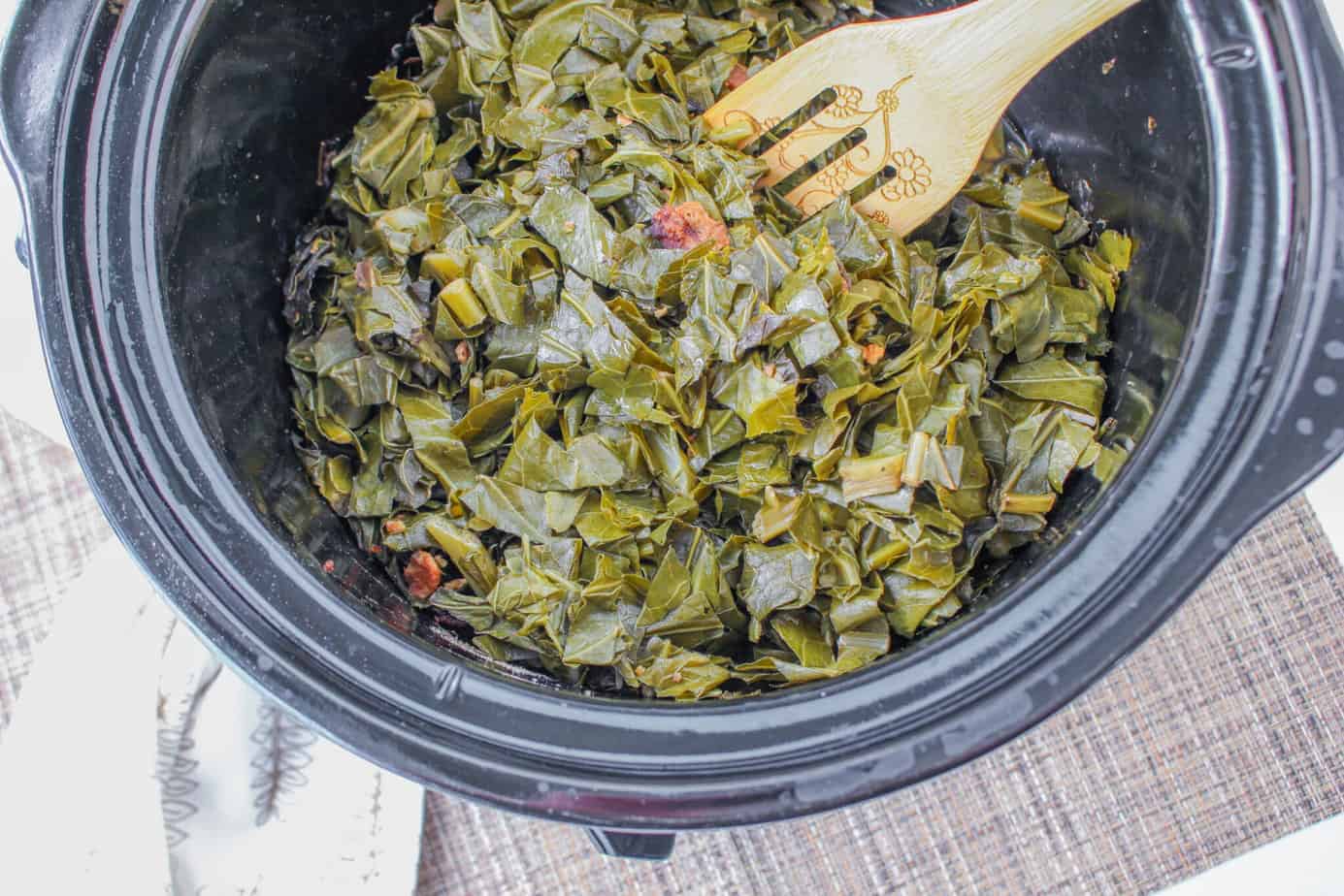 Easy Crockpot Collard Greens in a slow cooker with a wooden slotted spoon