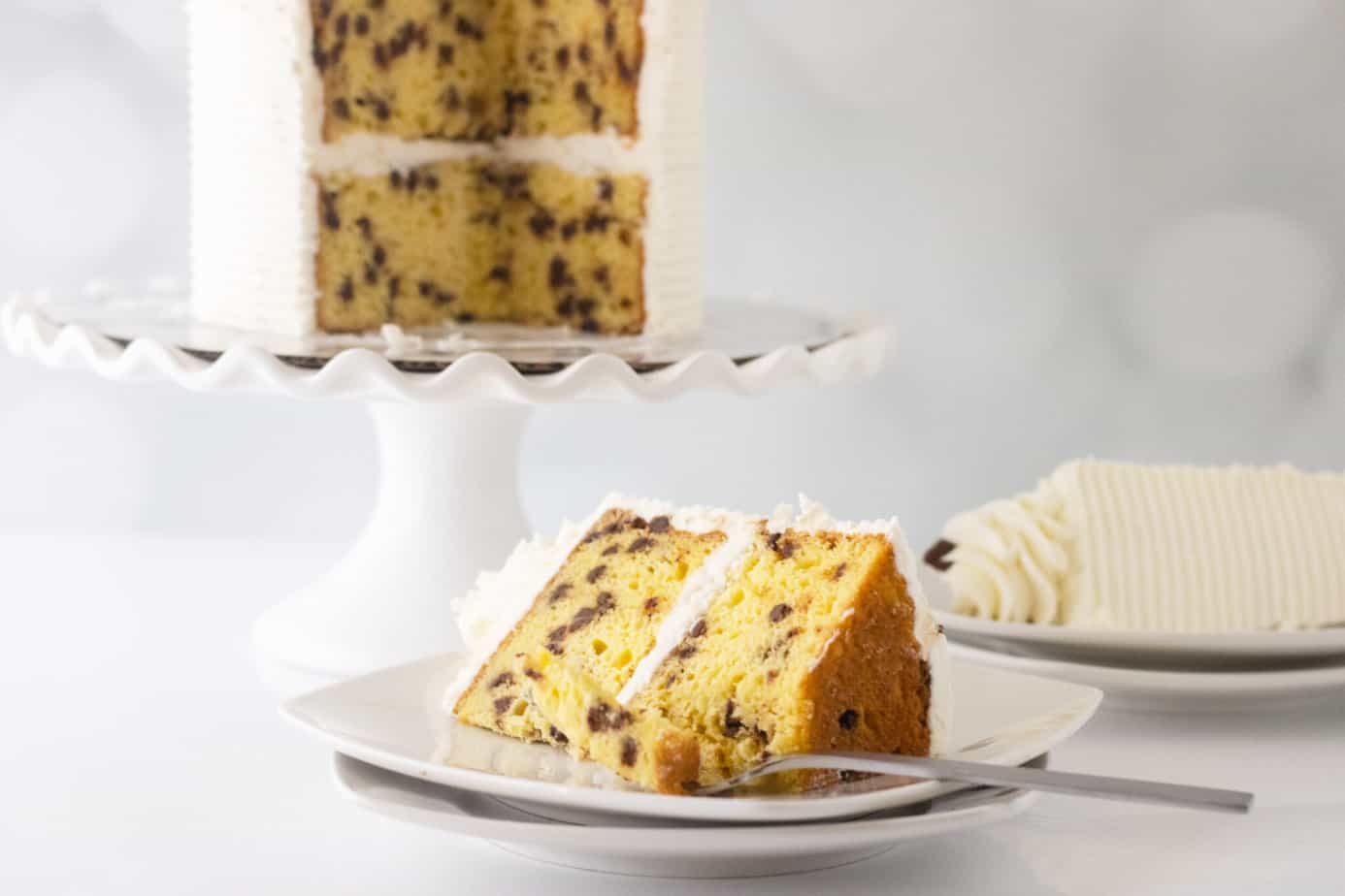 a slice of cake with chocolate chips and vanilla buttercream on a white plate