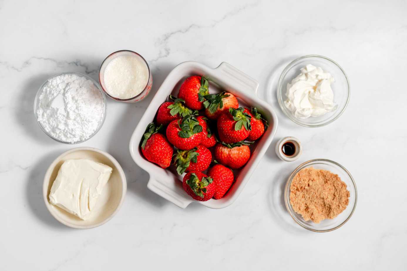 deviled strawberries ingredients in white and clear bowls on a white counter