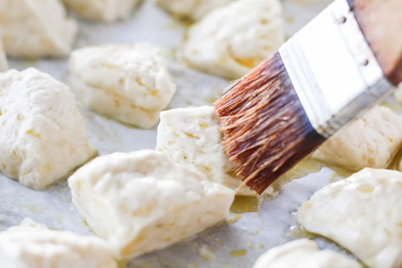 brushing butter over water dipped biscuit dough on parchment paper