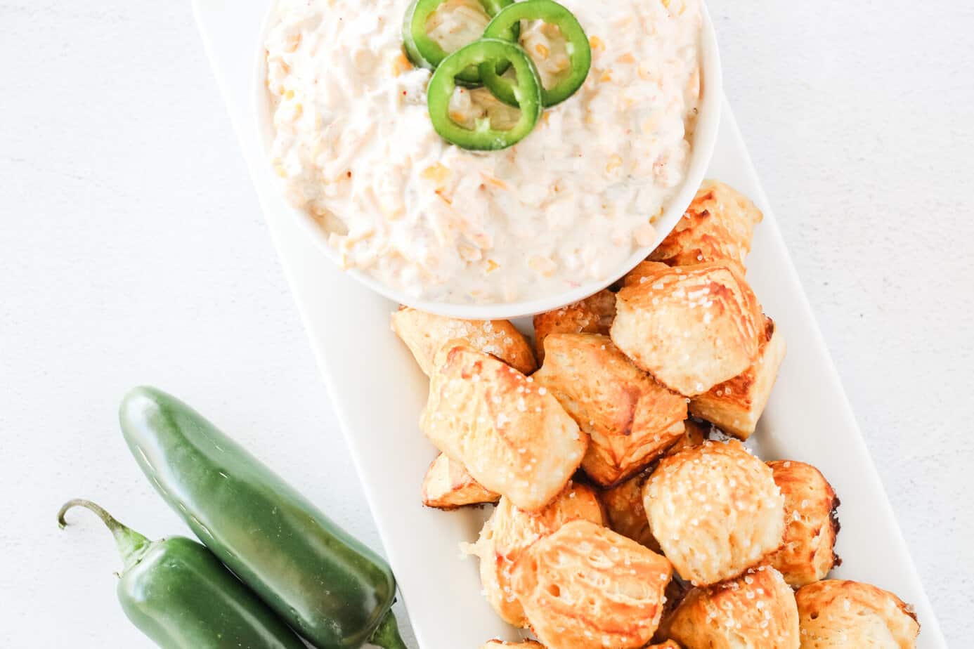 pretzel bites from biscuits on a white platter with corn dip and jalapenos on the counter next to the dish