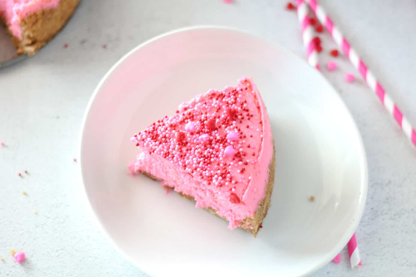 a slice of hot pink valentine's day cheesecake with red pink and white sprinkles on a white plate