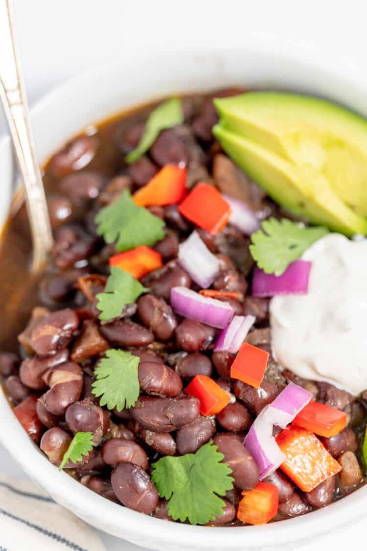 instant pot black bean soup in bowls with avocado, sour cream, peppers and onions for toppings
