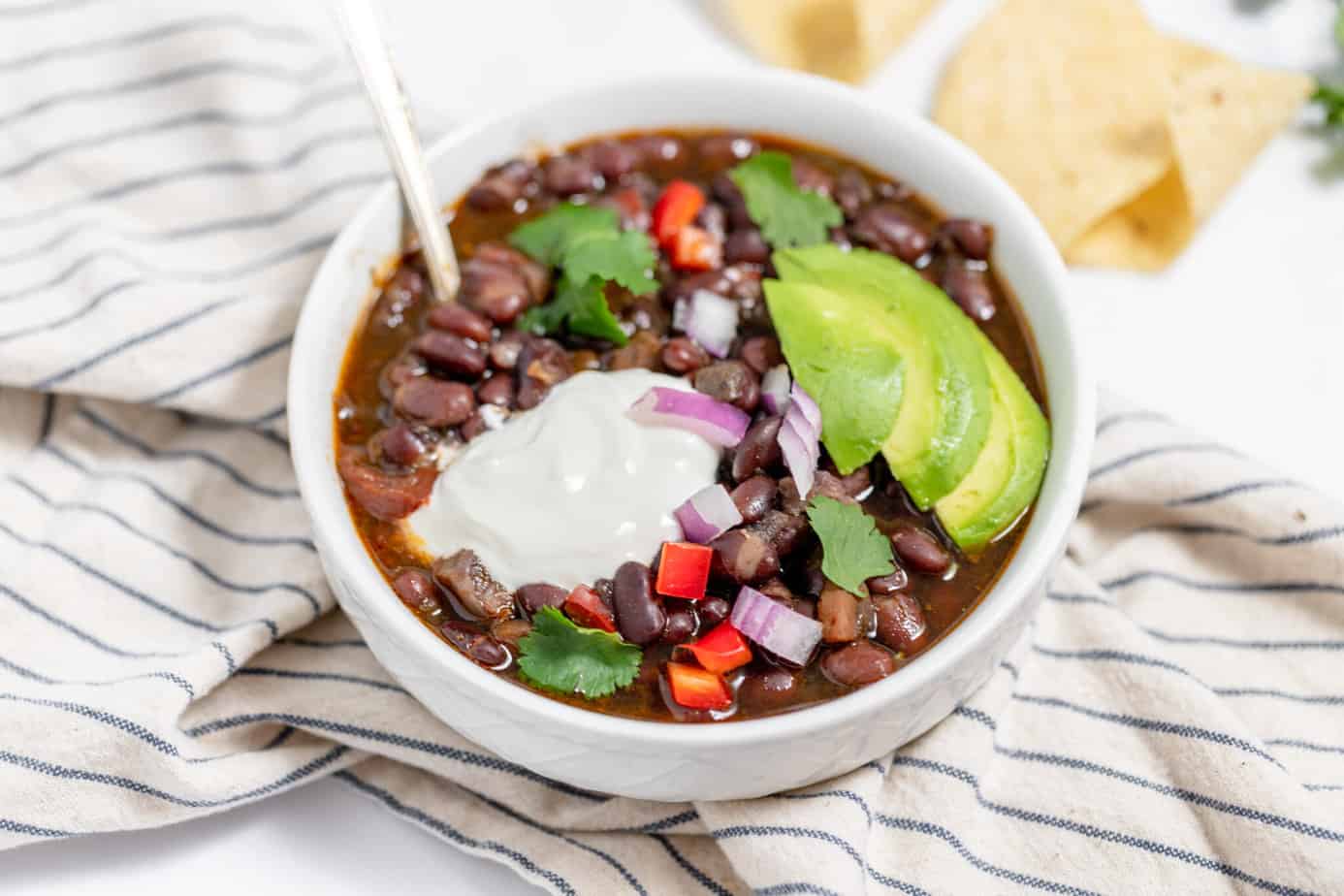 instant pot black bean soup in bowls with avocado, sour cream, peppers and onions for toppings