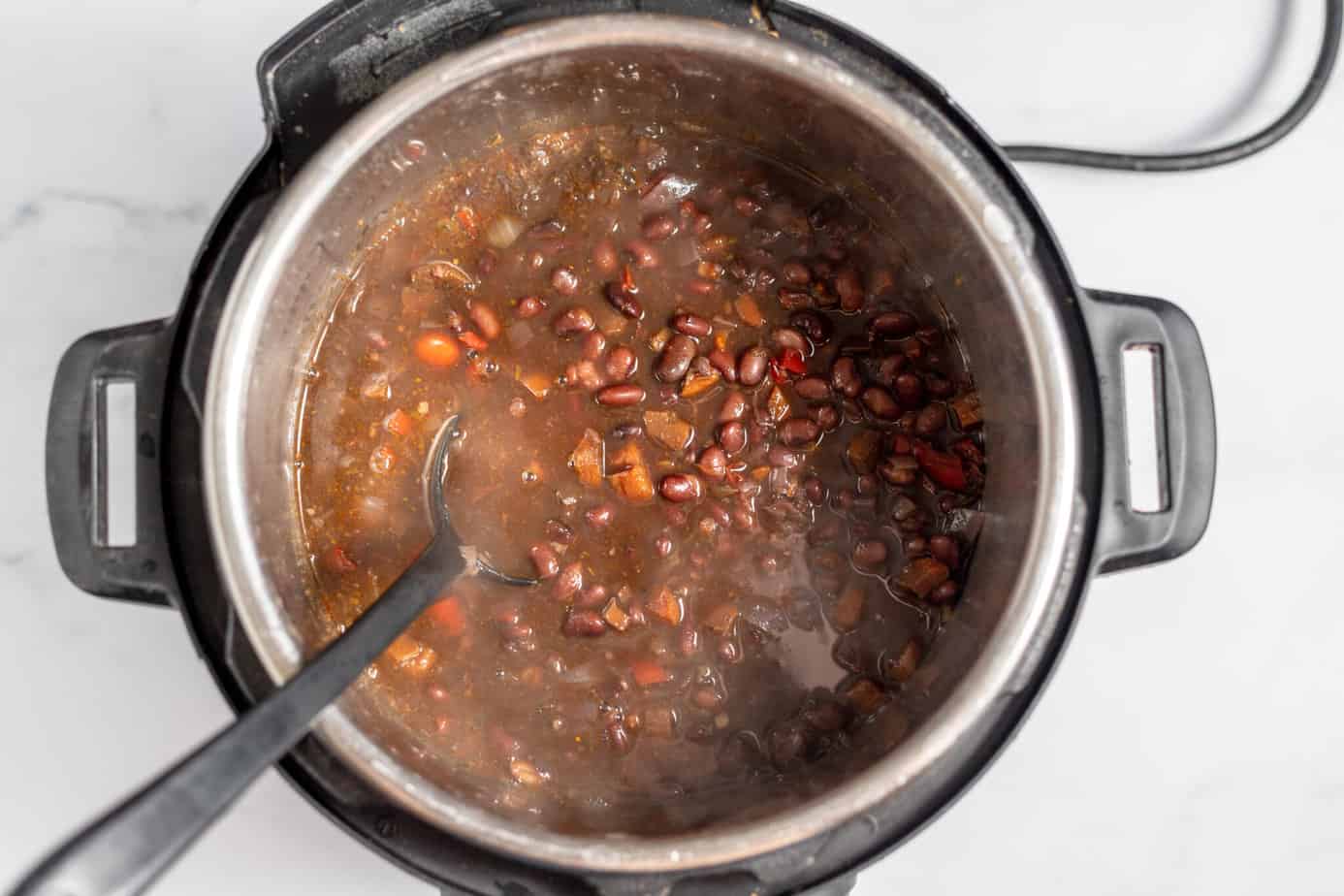 finished instant pot black bean soup still in the pressure cooker with a black spoon