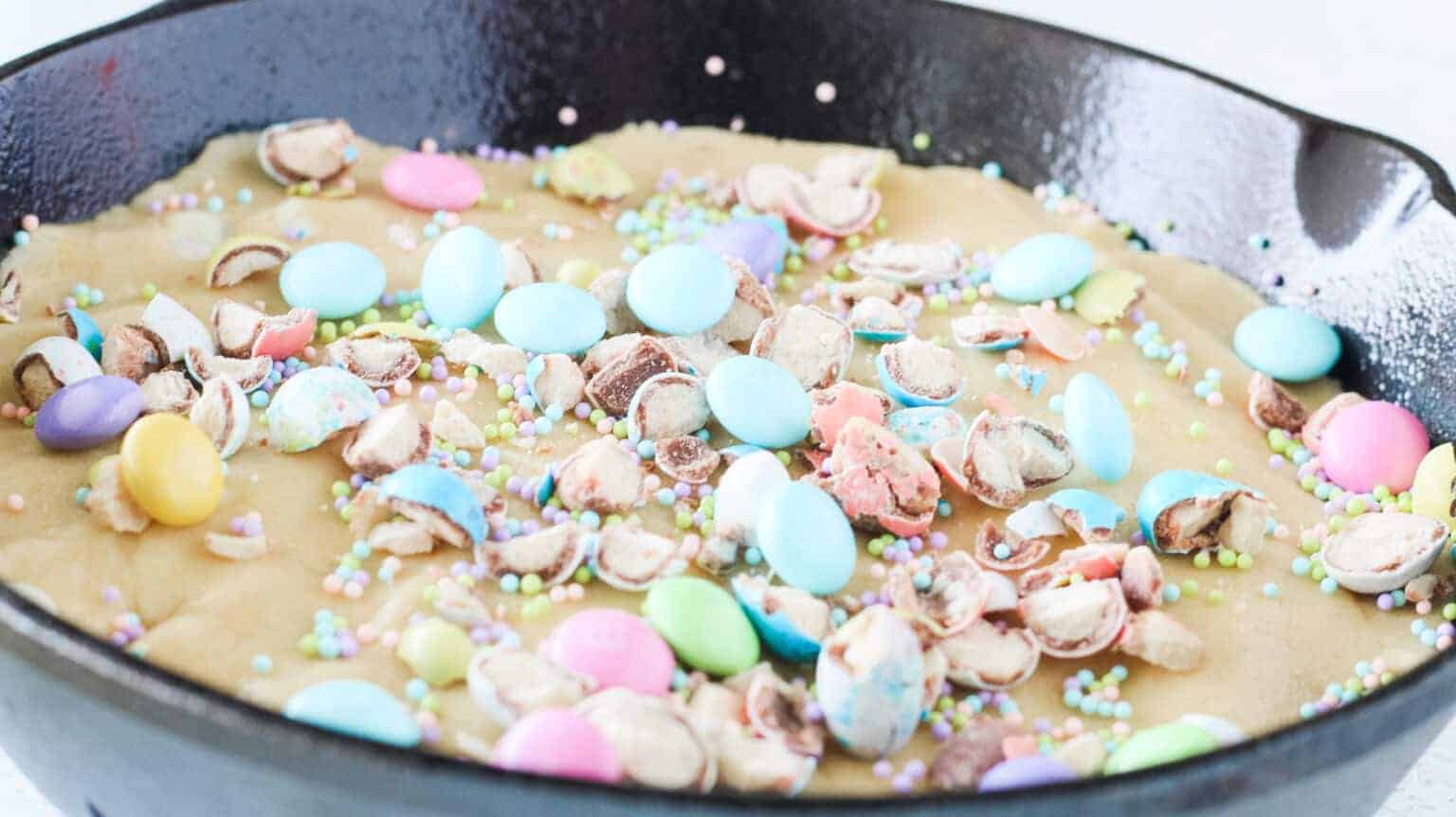 sprinkles, m&M's and malted milk eggs crushed and placed on top of easter skillet cookie dough in skillet