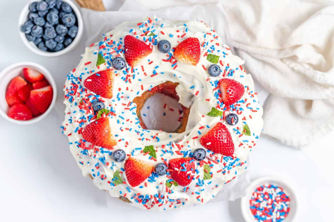 cream cheese glaze on pound cake with strawberries and blueberries on top plus red white and blue sprinkles