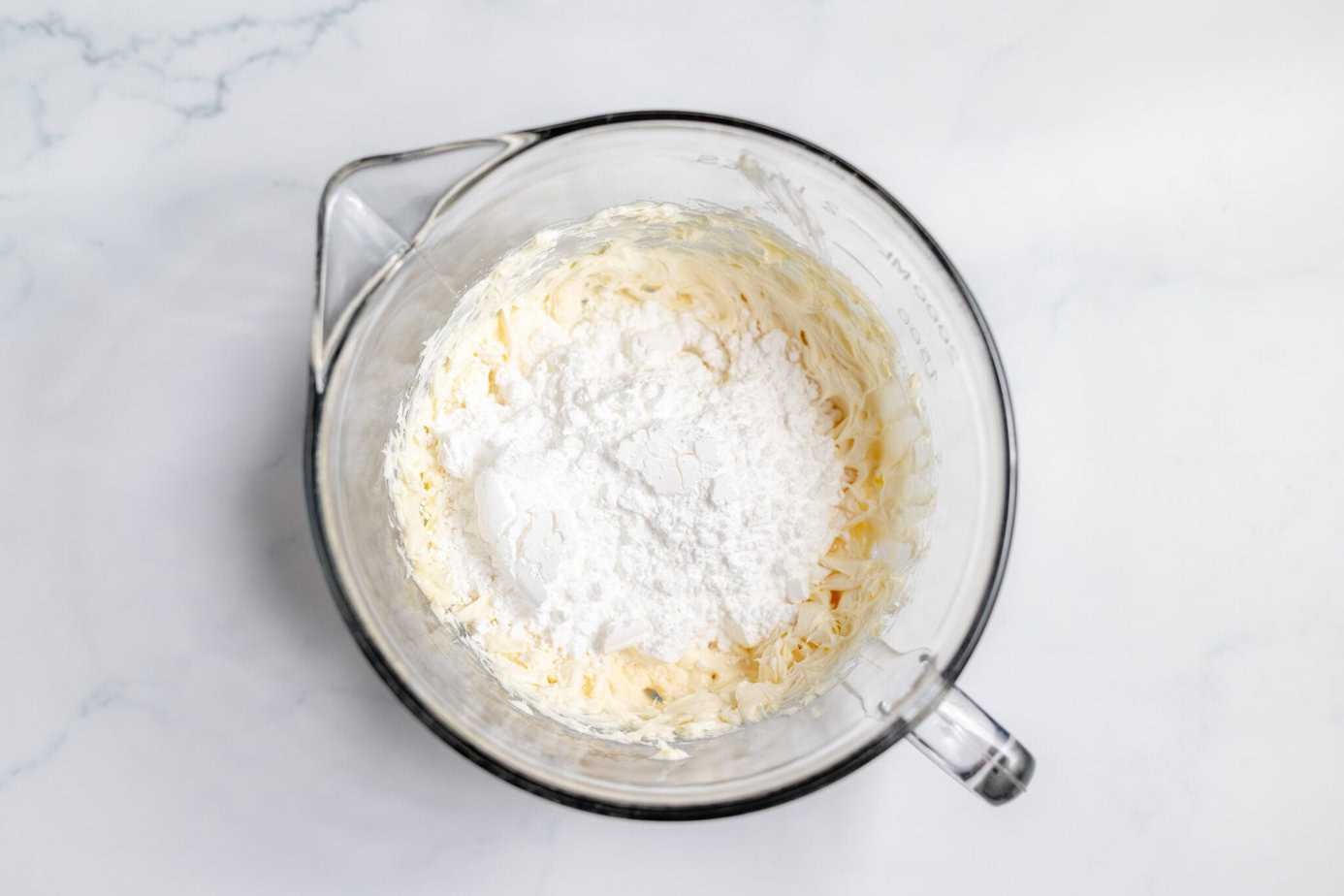 creamed cream cheese and butter in mixing bowl with powdered sugar on top