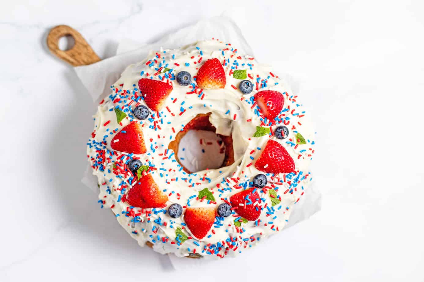 cream cheese glaze on pound cake with strawberries and blueberries on top plus red white and blue sprinkles