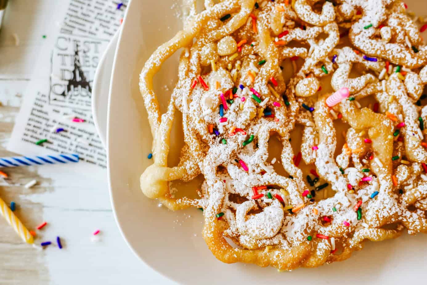 funnel cake on a plate with sprinkles and powdered sugar