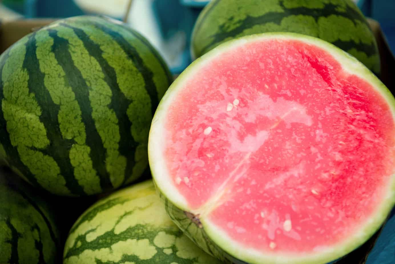 pile of watermelons with one sliced open to show the pink inside.