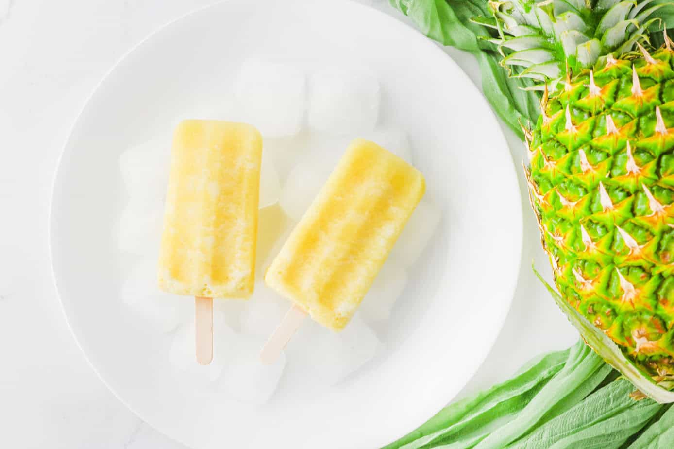 pina colada popsicles on a white plate with ice