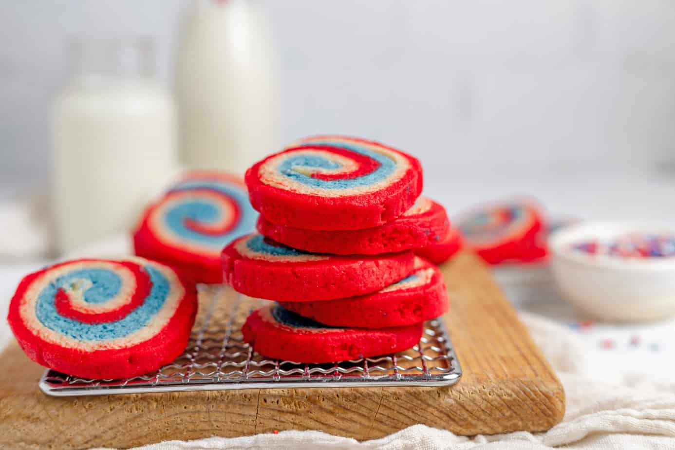 4th of July Cookies (Red White and Blue Pinwheel Cookies) stacked on a wire rack that is resting on a wooden cutting board