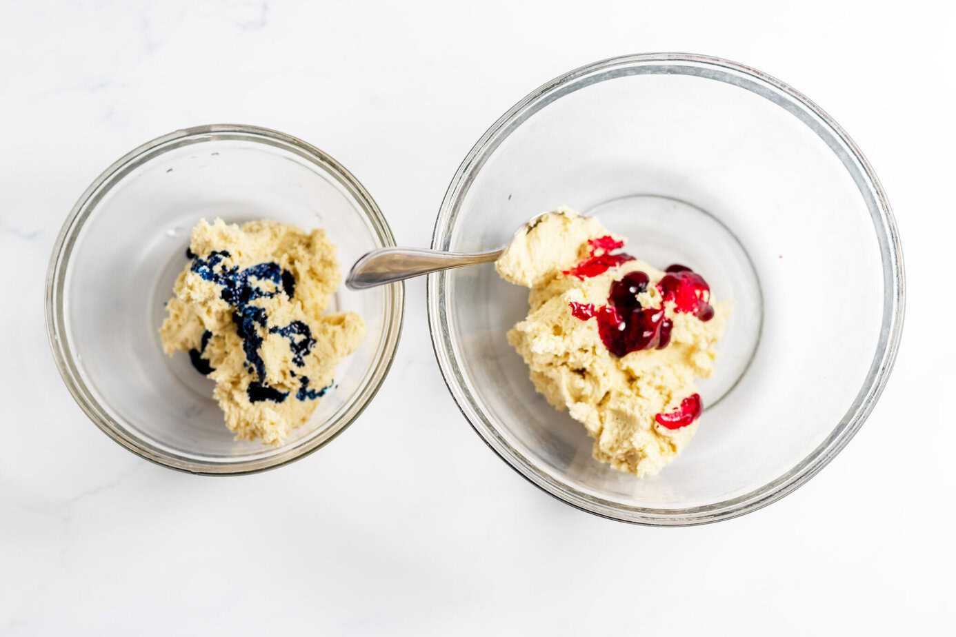 two balls of cookie dough in separate bowls - one with blue coloring and one with red coloring
