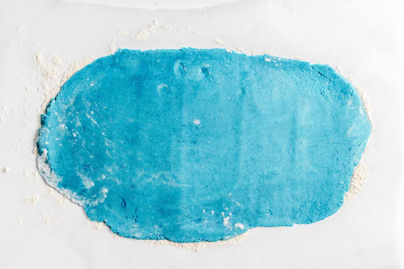 blue cookie dough rolled out on parchment paper