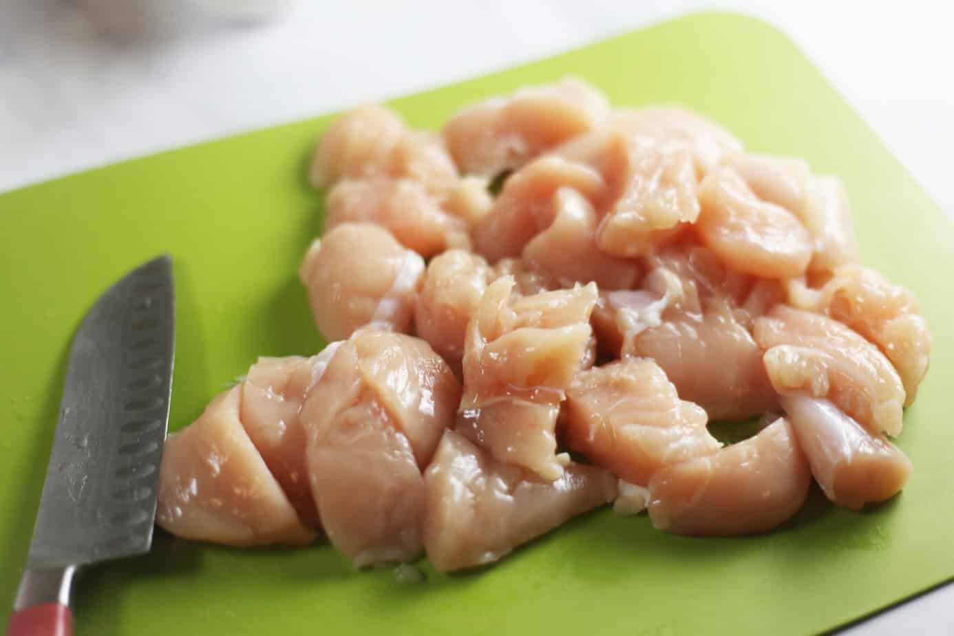 chicken breasts cut into chunks on a green cutting board