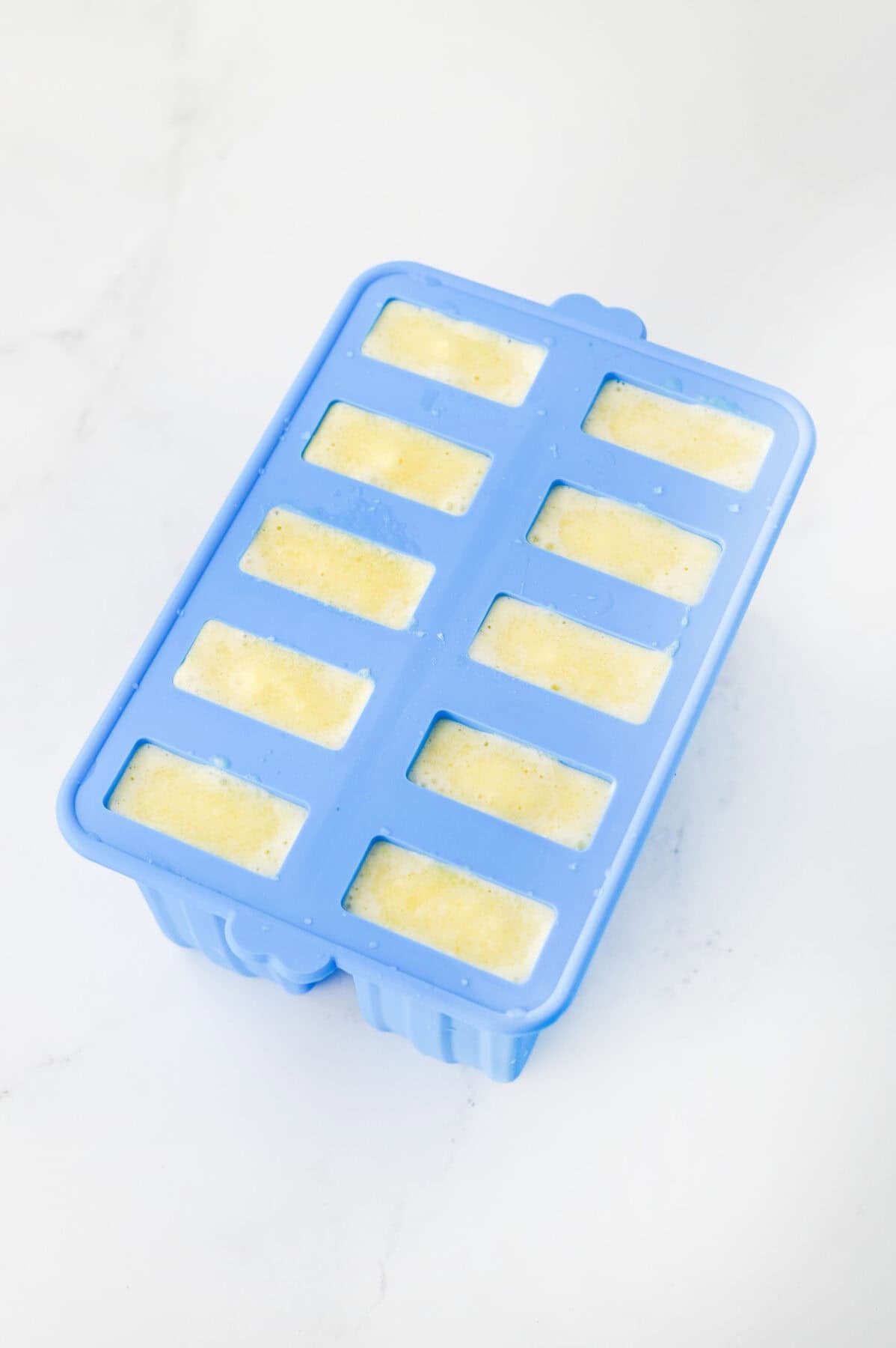 blended ingredients for pina colada popsicles poured into popsicle molds