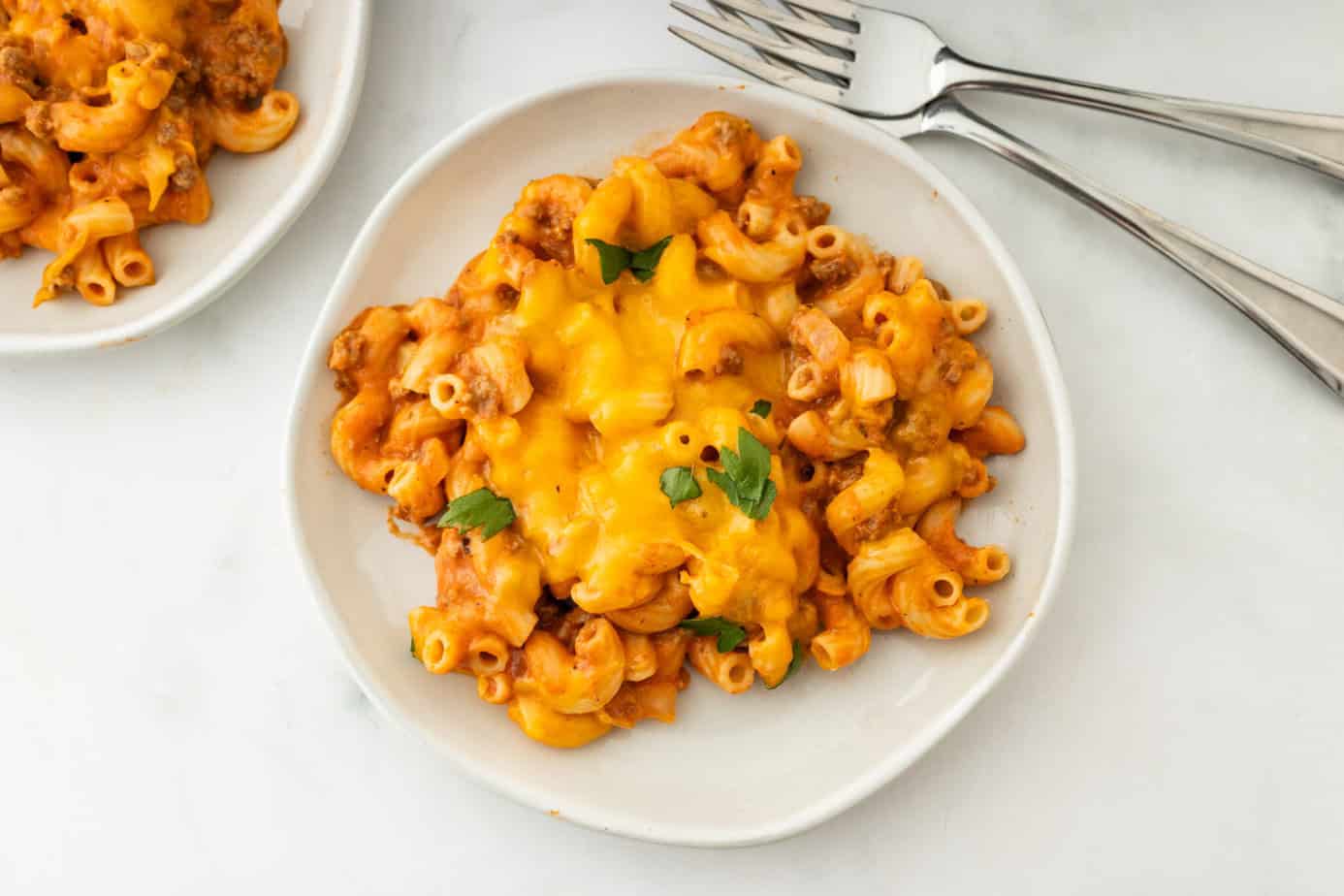 cheesy beefaroni recipe on a white plate with bread