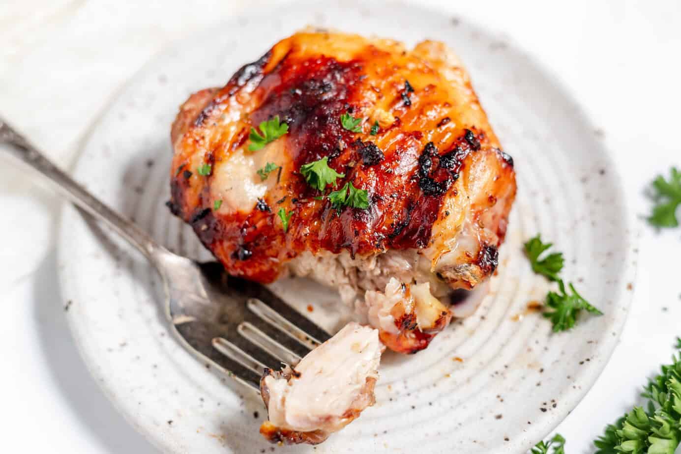 grilled chicken thigh on a plate with a bite on a fork next to it