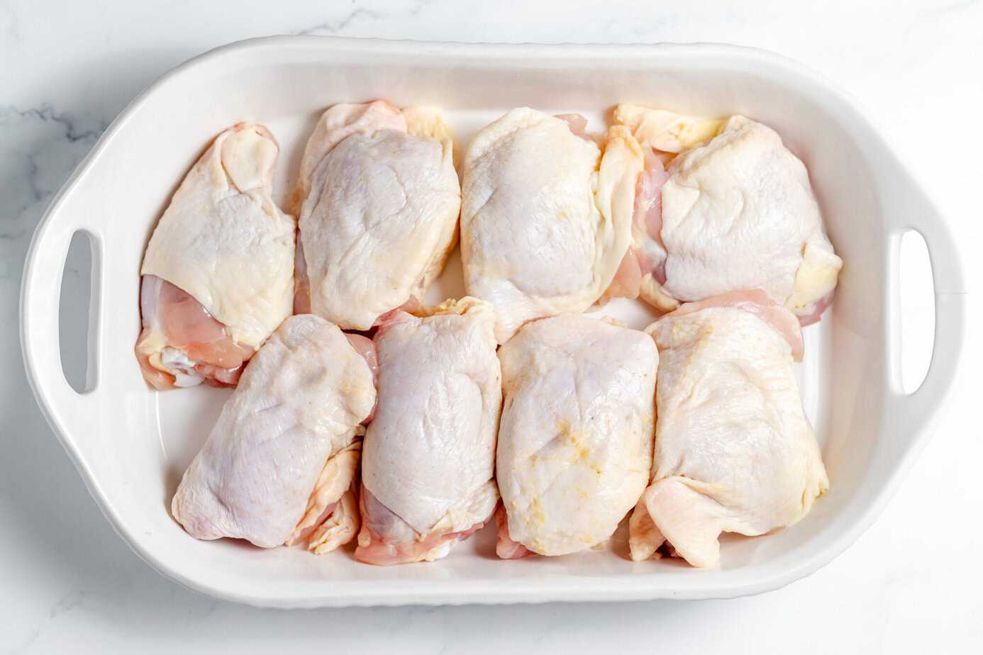raw chicken thighs in shallow white baking dish