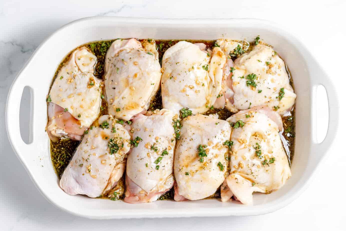 raw chicken thighs in shallow white baking dish with marinade poured over top of the chicken