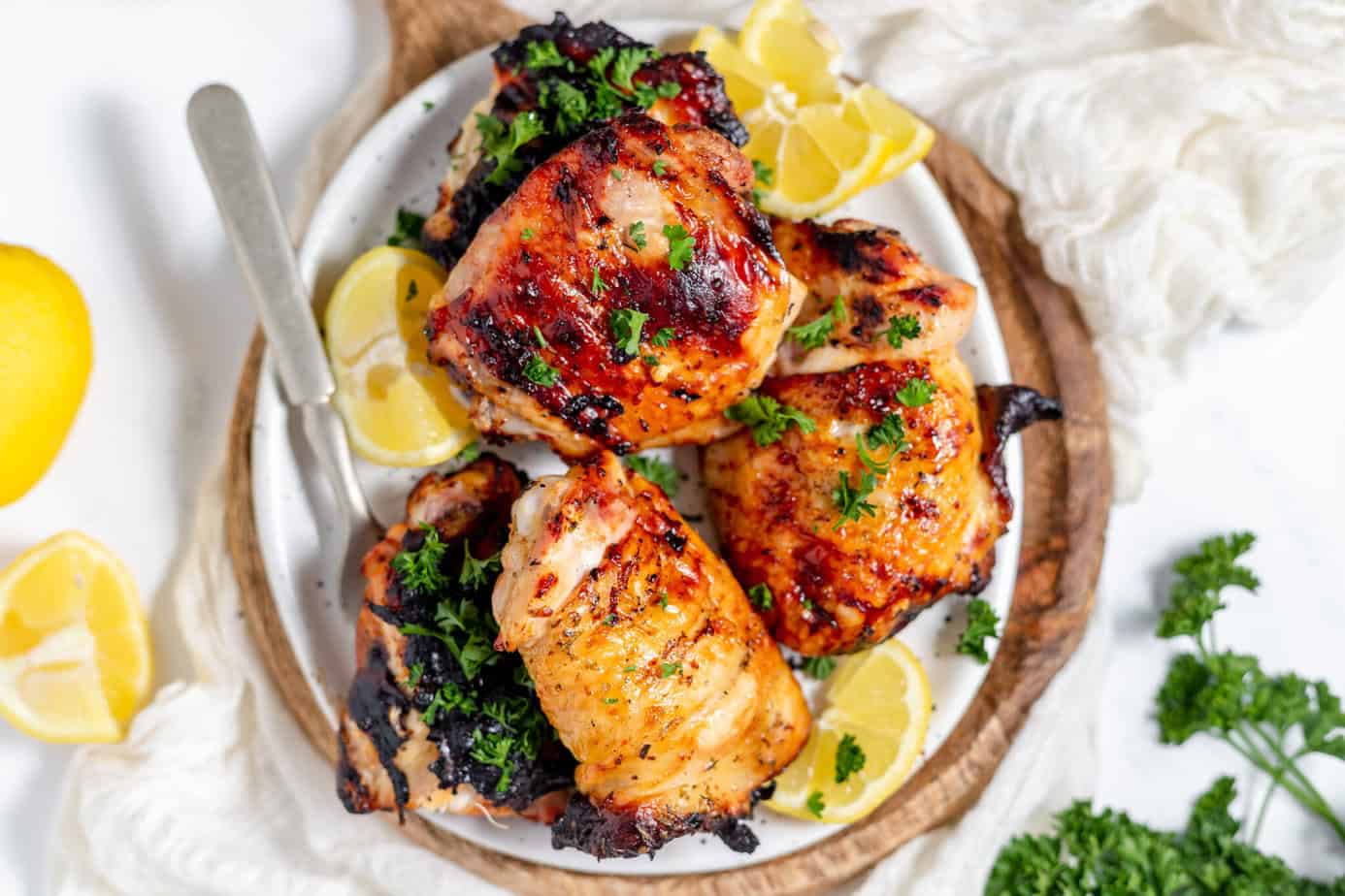 grilled chicken thighs on a white plate with lemon wedges and parsley
