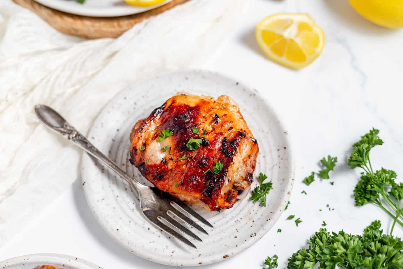 grilled chicken thigh on a white plate with a fork and parsley