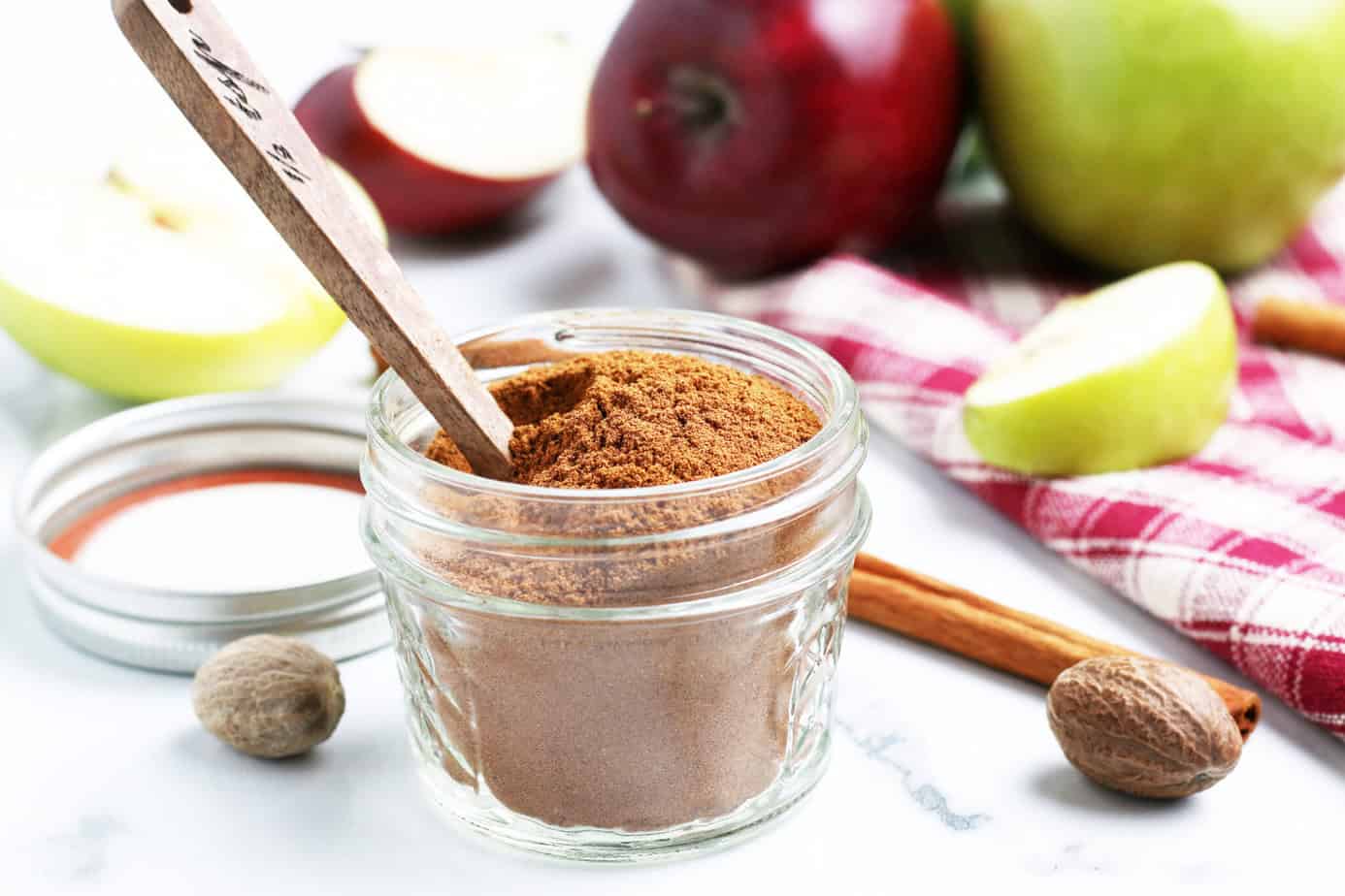homemade apple pie spice in a clear jar with a wooden teaspoon