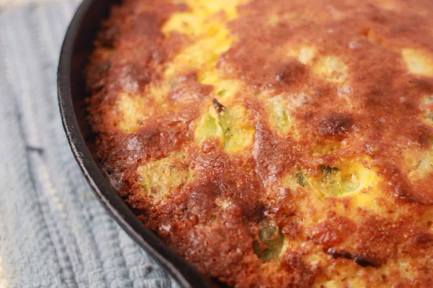 cooked broccoli cheese cornbread in skillet on a blue placemat